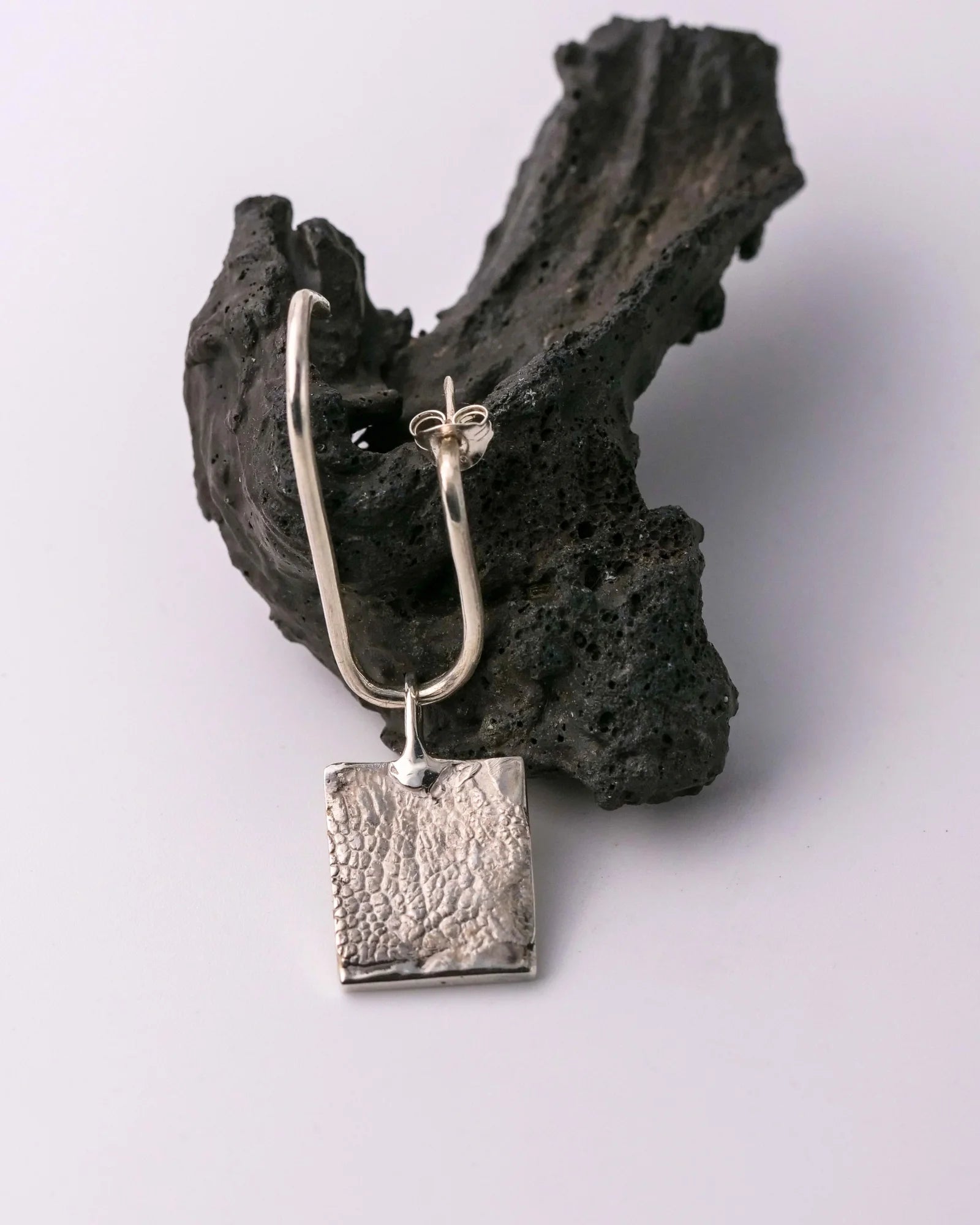 Pendentif carré en argent avec empreinte animale présenté sur une boucle d'oreille.