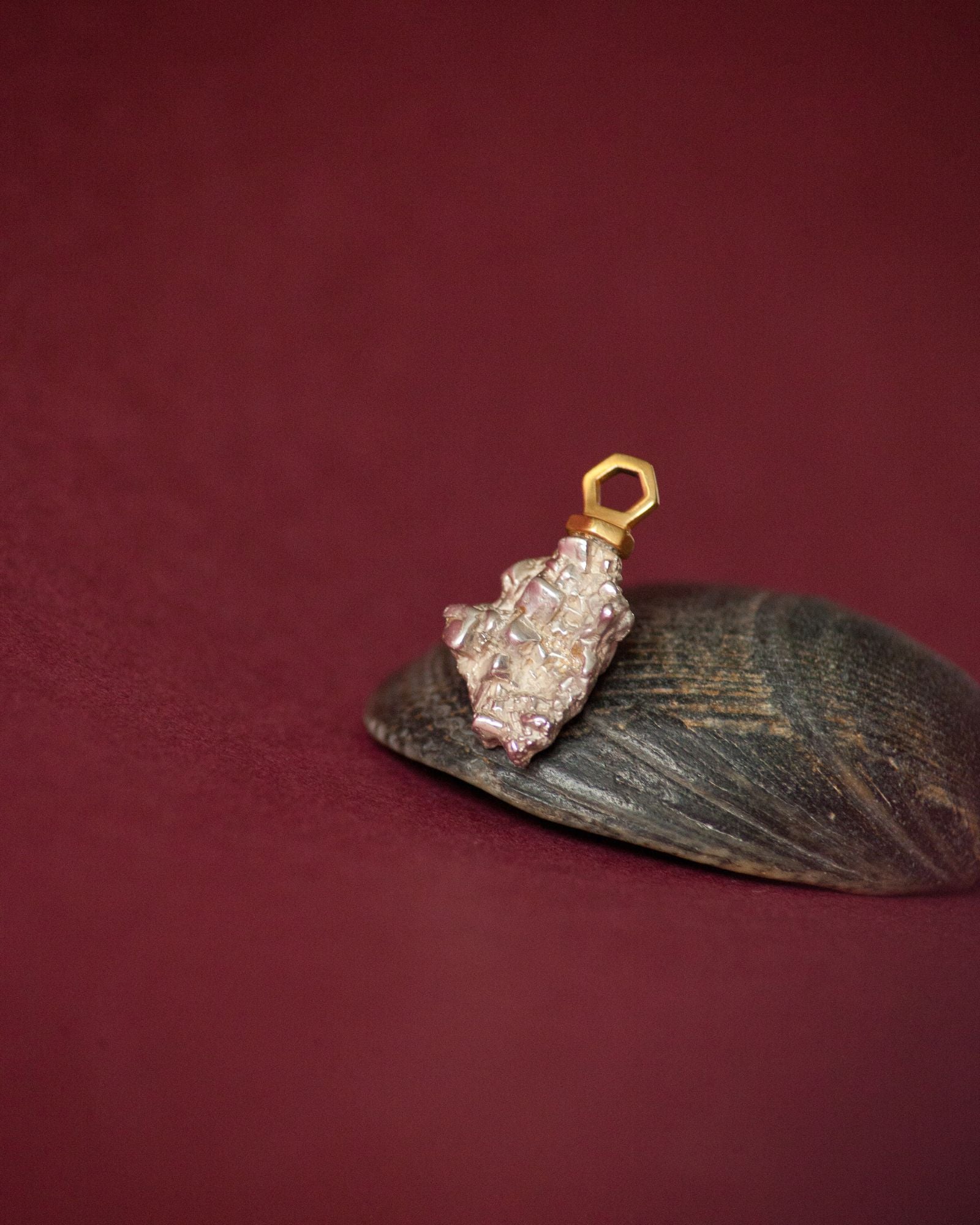 Photo d'un pendentif éthique en vermeil labellisé serti d'une pépite en argent labellisé, sur fond bordeaux avec support coquillage noir.