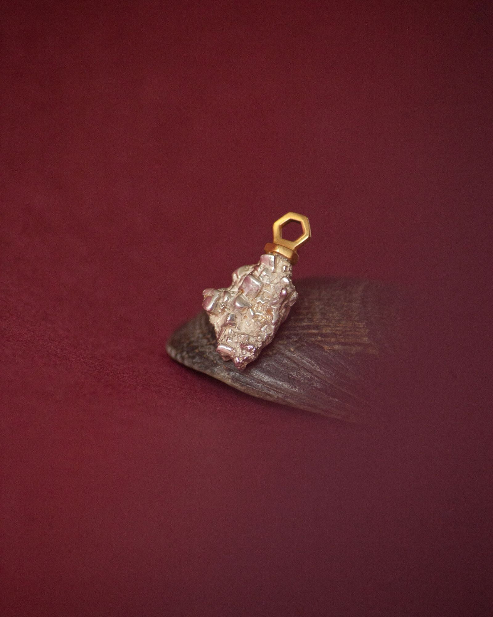 Photo d'un pendentif éthique en vermeil labellisé serti d'une pépite en argent labellisé, sur fond bordeaux avec support coquillage noir, effet flou de la couleur de fond.