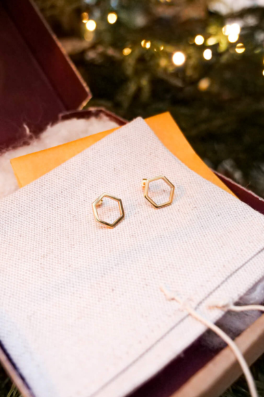 Boucles d'oreilles éthiques modèles Essentiel 14, forme hexagonale en or jaune non portées présentées dans le packaging avec en fond les lumières de noël.