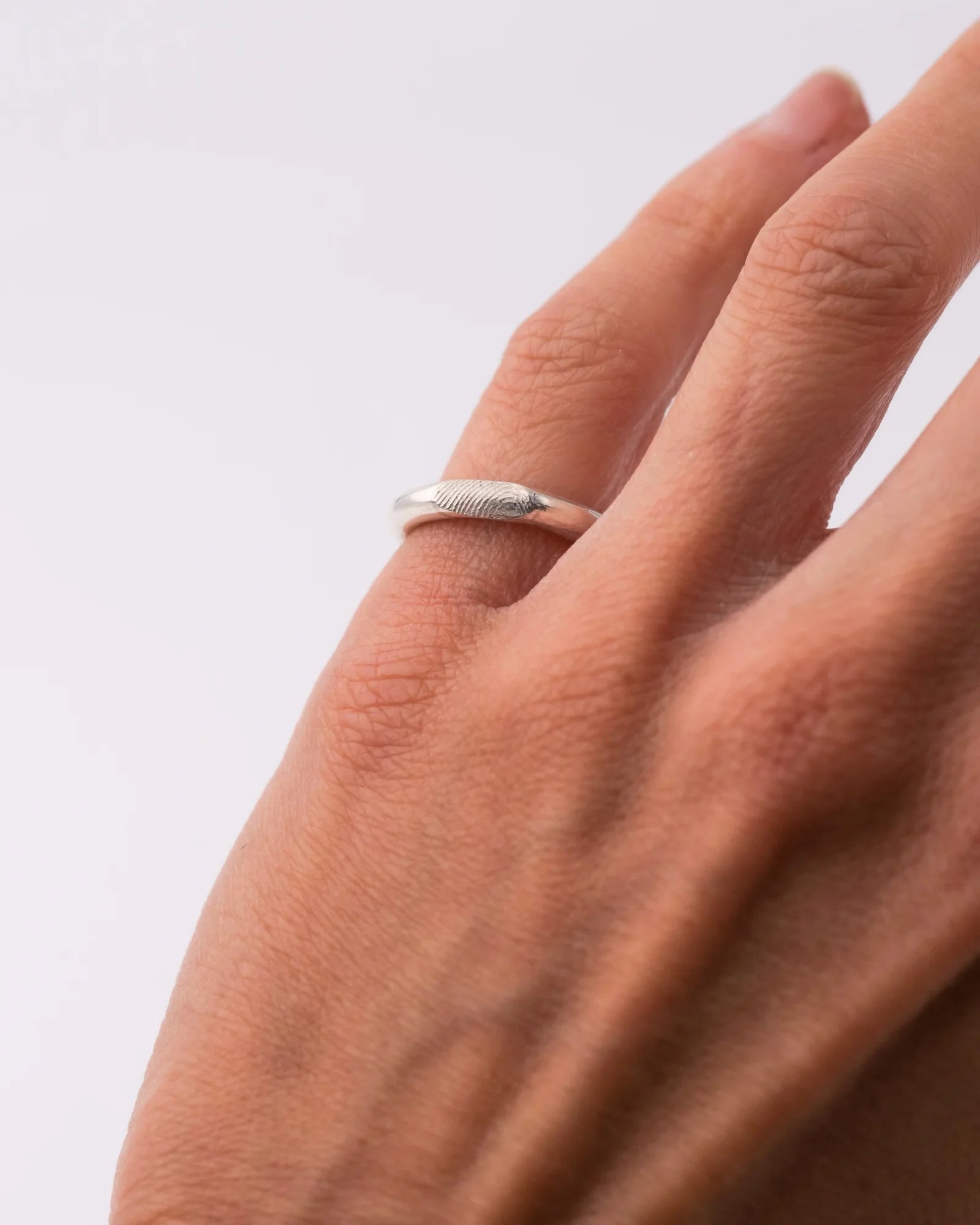 Bague en argent portée  l'auriculaire avec empreinte digitale.