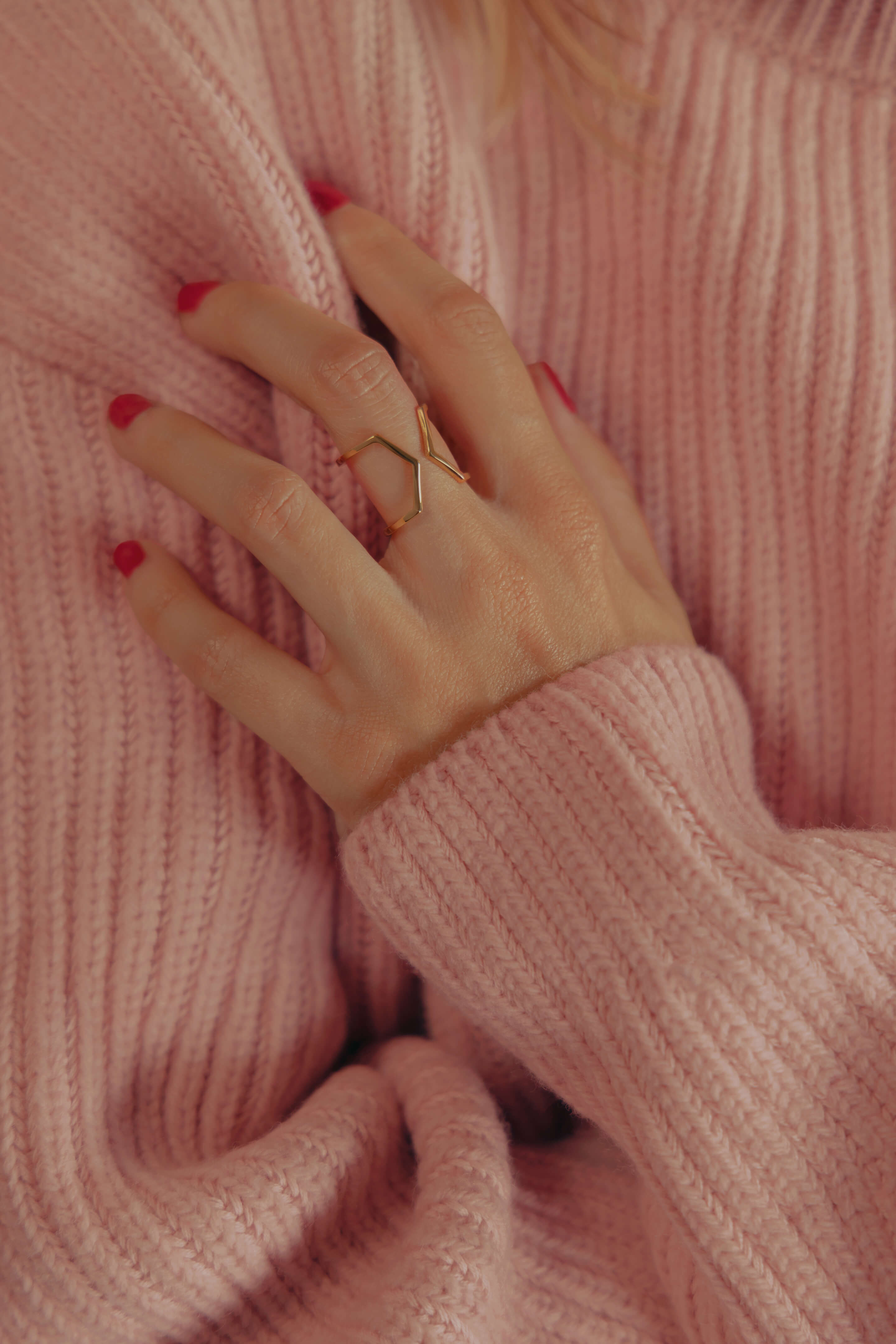 Photo d'une bague éthique portée à la main, modèle Dualité Large en or jaune fairmined, sur fond pull rose.