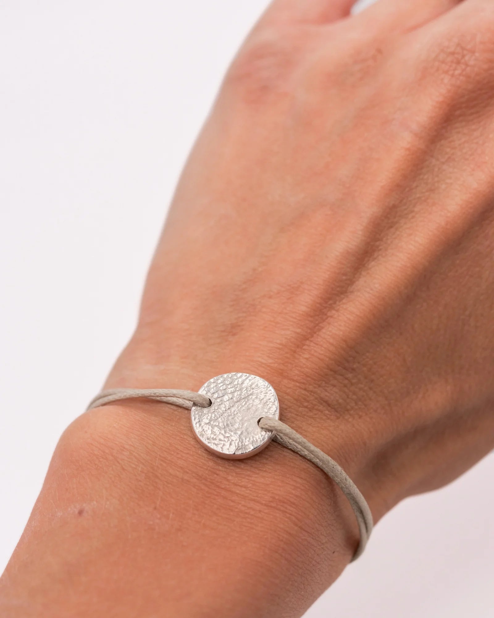 Bracelet cordon avec médaille ronde en argent avec empreinte animale porté.