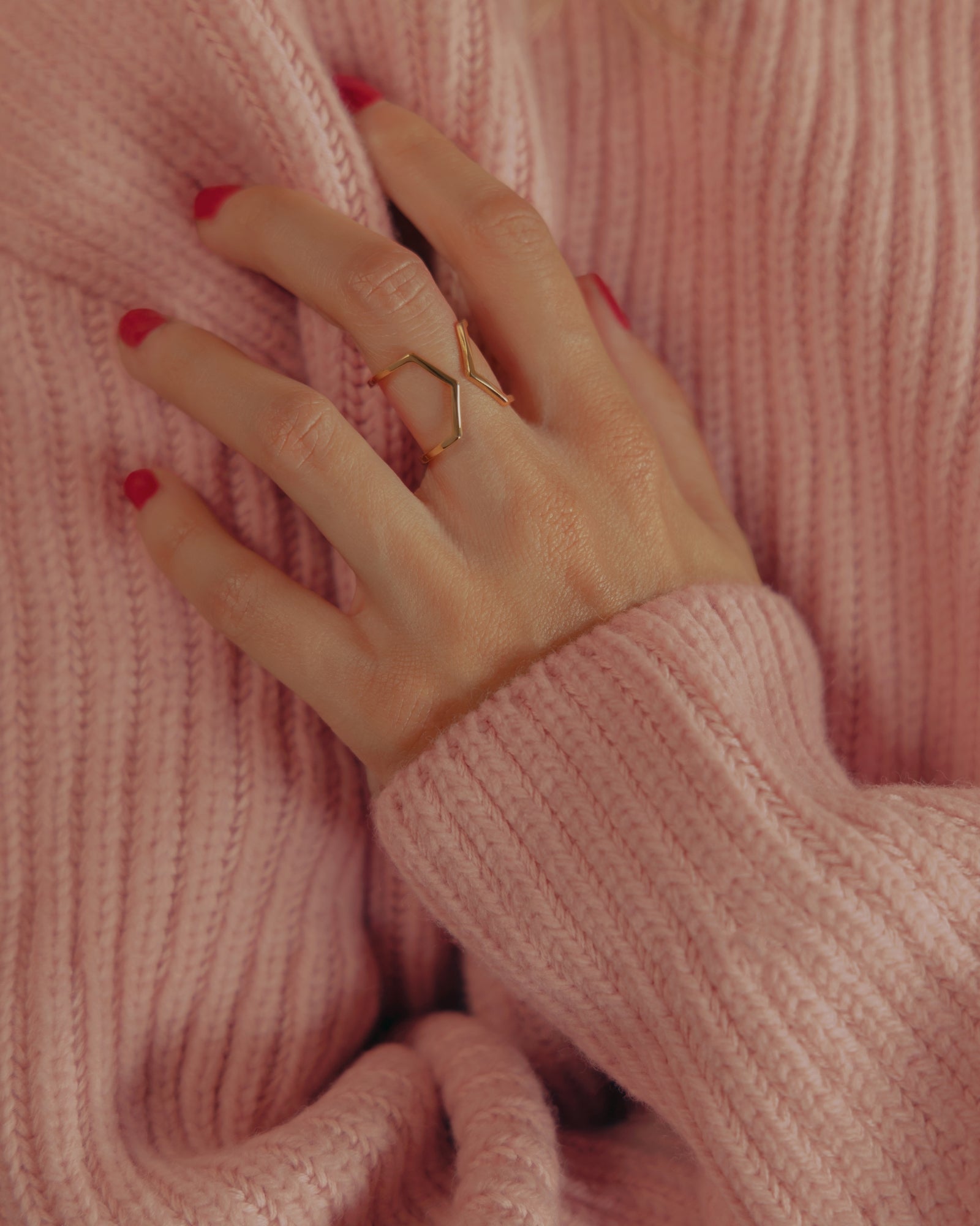 Photo d'une bague éthique portée à la main, modèle Dualité Large en vermeil, sur fond pull rose.