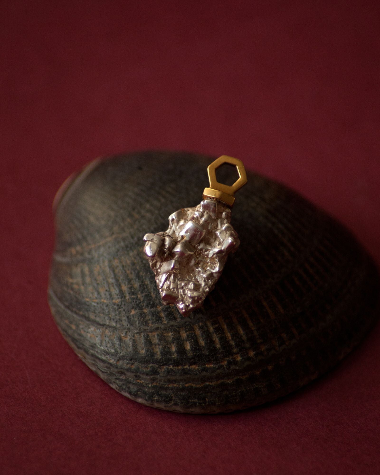 Photo d'un pendentif éthique en vermeil labellisé serti d'une pépite en argent  labellisé, sur fond bordeaux avec support coquillage noir.
