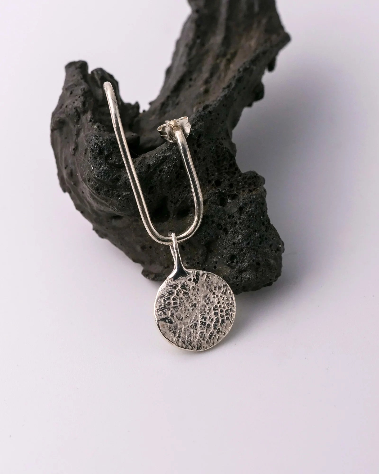 Pendentif rond en argent avec empreinte animale présenté sur une boucle d'oreille.