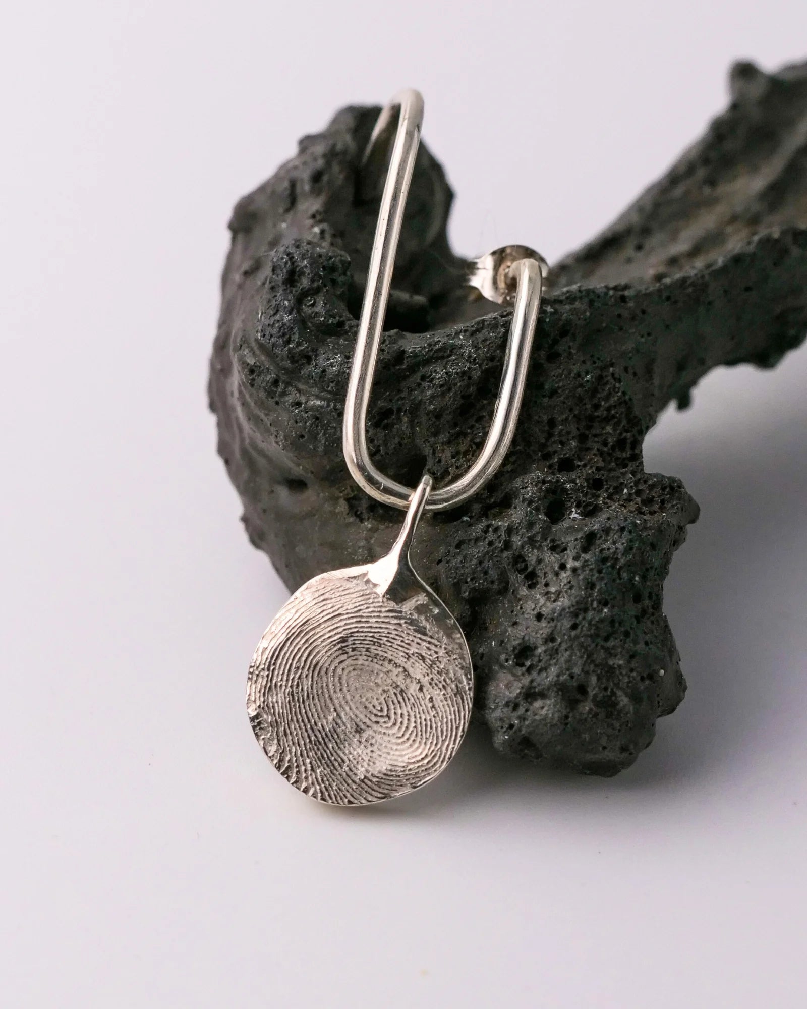 Pendentif rond en argent avec empreinte digitale sur boucle d'oreille.