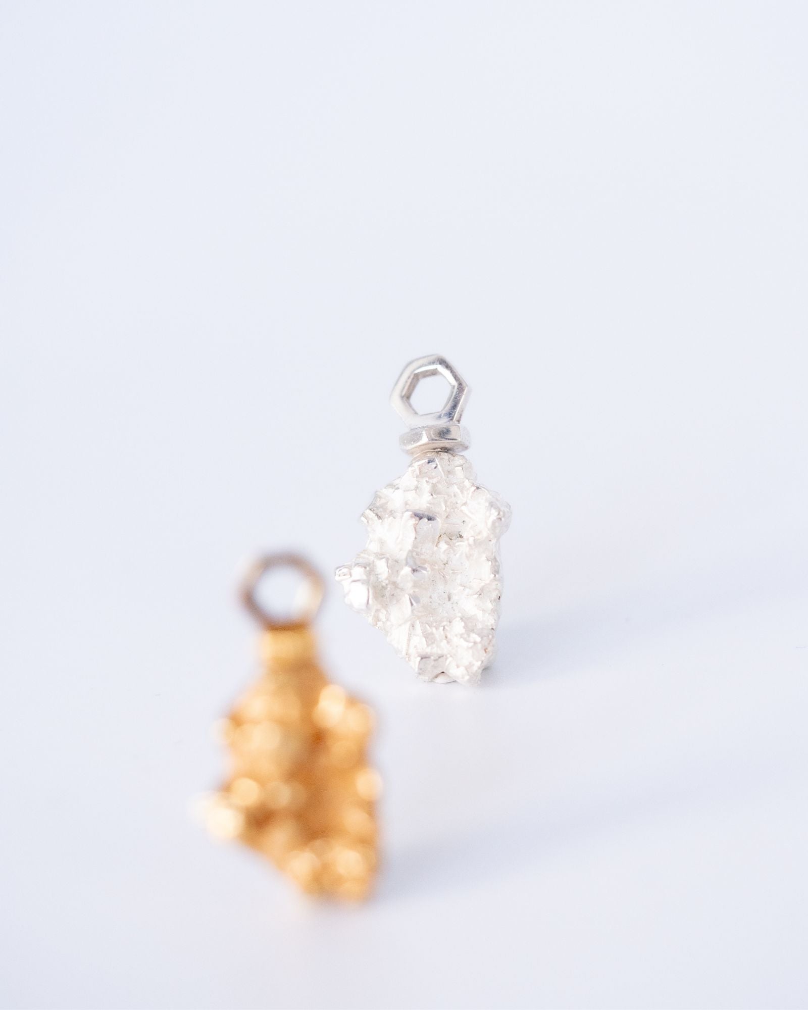 Photo d'un pendentif en argent éthique, recyclé et labellisé, modèle Infime pépite, reprenant l'ésthetique d'une pierre brute. en premier plan flouté apparait le même pendentif en vermeil.